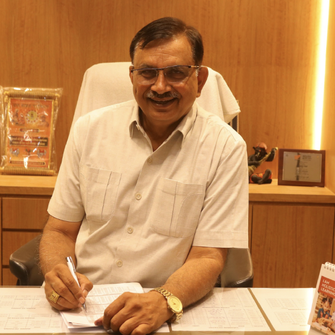 Man in a light shirt sits at a desk, signing papers in an office setting with wooden paneling and a gold watch visible on his wrist
